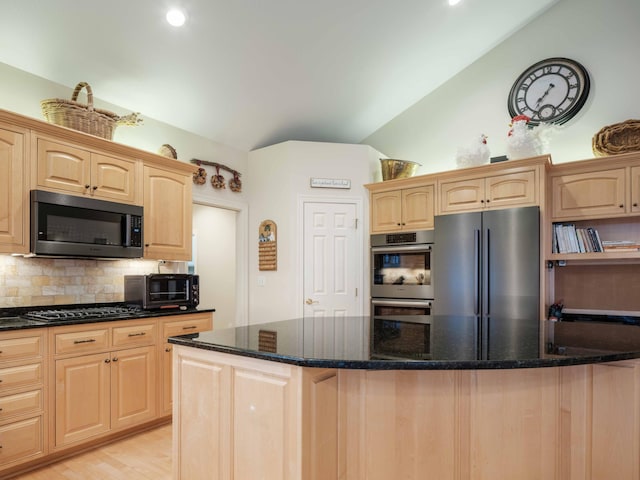 kitchen with dark stone countertops, light brown cabinets, vaulted ceiling, and appliances with stainless steel finishes