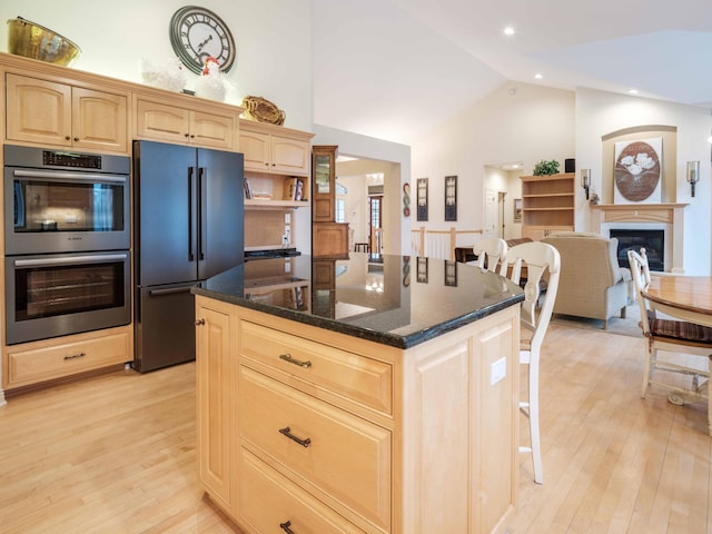 kitchen with dark stone counters, high end refrigerator, light wood-type flooring, double oven, and a kitchen island