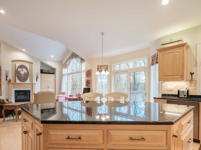 kitchen with a center island, light brown cabinets, hanging light fixtures, light hardwood / wood-style flooring, and dark stone countertops