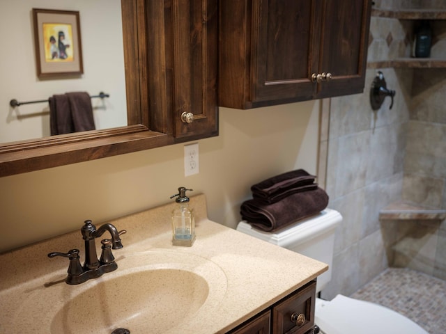 bathroom featuring a tile shower, vanity, and toilet