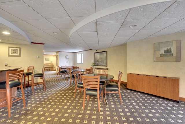 dining room featuring a drop ceiling, dark colored carpet, and radiator heating unit