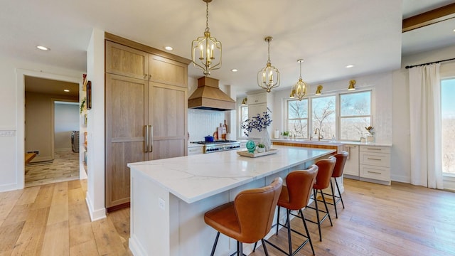 kitchen with premium range hood, hanging light fixtures, a center island, and light hardwood / wood-style floors