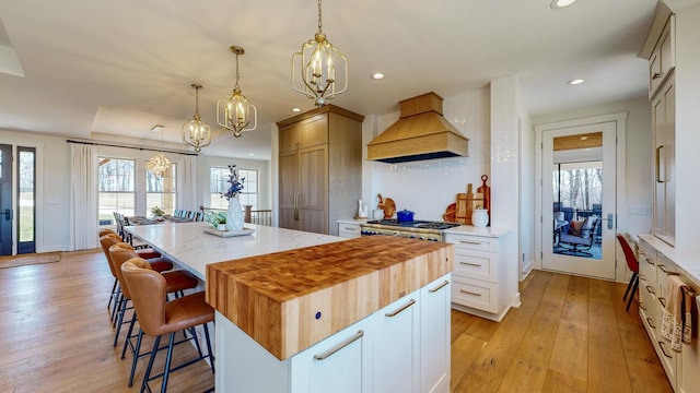 kitchen featuring a large island, light hardwood / wood-style floors, pendant lighting, white cabinets, and custom exhaust hood