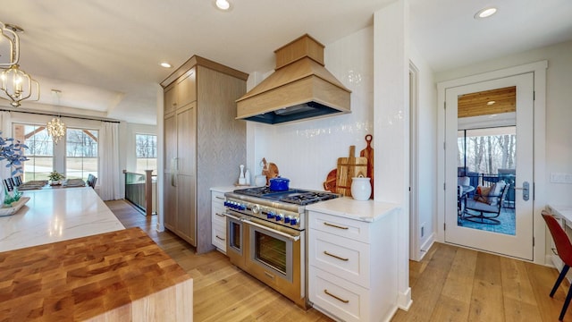 kitchen featuring light hardwood / wood-style flooring, a notable chandelier, decorative light fixtures, range with two ovens, and custom exhaust hood