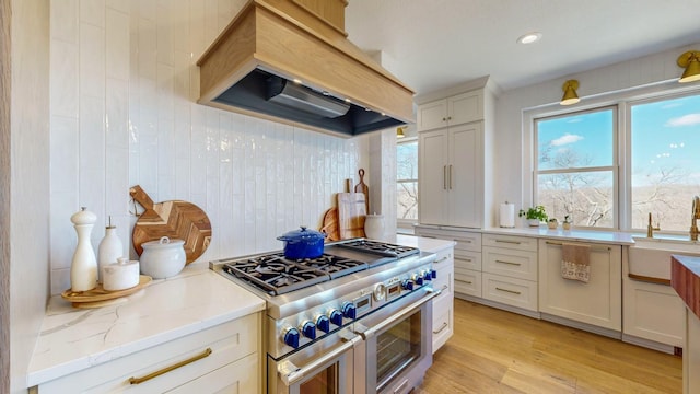 kitchen featuring white cabinets, stainless steel stove, light hardwood / wood-style floors, light stone counters, and custom range hood