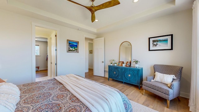 bedroom with light hardwood / wood-style floors, a raised ceiling, and ceiling fan