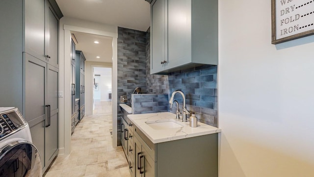 kitchen featuring gray cabinetry, sink, decorative backsplash, light stone countertops, and washer / dryer