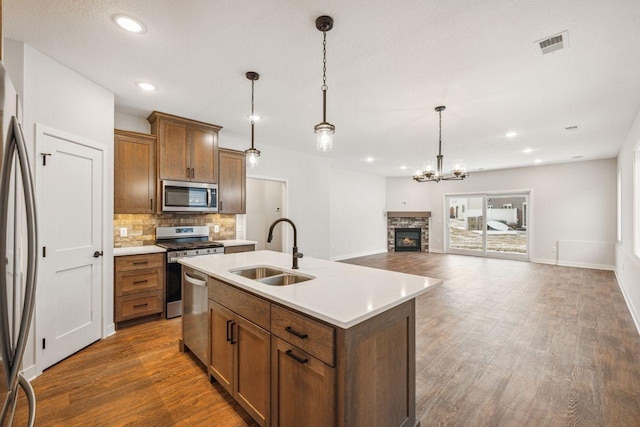 kitchen with appliances with stainless steel finishes, decorative light fixtures, sink, backsplash, and a center island with sink