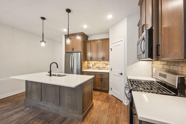 kitchen featuring sink, hanging light fixtures, appliances with stainless steel finishes, dark hardwood / wood-style floors, and an island with sink