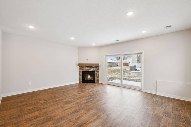 unfurnished living room with a stone fireplace, dark hardwood / wood-style floors, and a textured ceiling