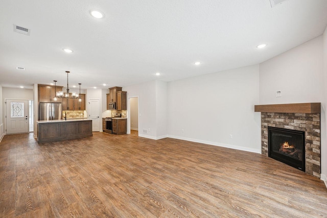 unfurnished living room with wood-type flooring, a brick fireplace, sink, and a notable chandelier