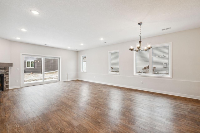 unfurnished living room featuring dark hardwood / wood-style flooring, a stone fireplace, a textured ceiling, and an inviting chandelier