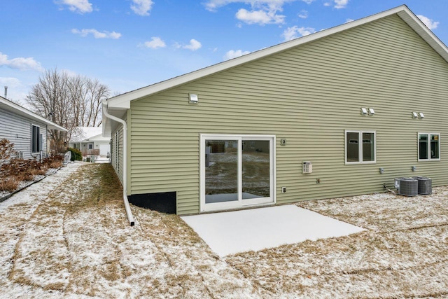 snow covered rear of property with a patio and central AC unit