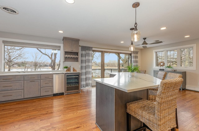 kitchen featuring decorative light fixtures, a breakfast bar area, beverage cooler, a water view, and light hardwood / wood-style flooring