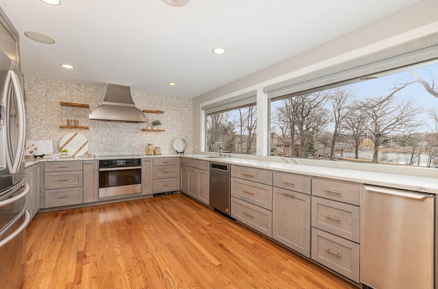 kitchen featuring wall chimney exhaust hood, sink, stainless steel appliances, light hardwood / wood-style floors, and backsplash