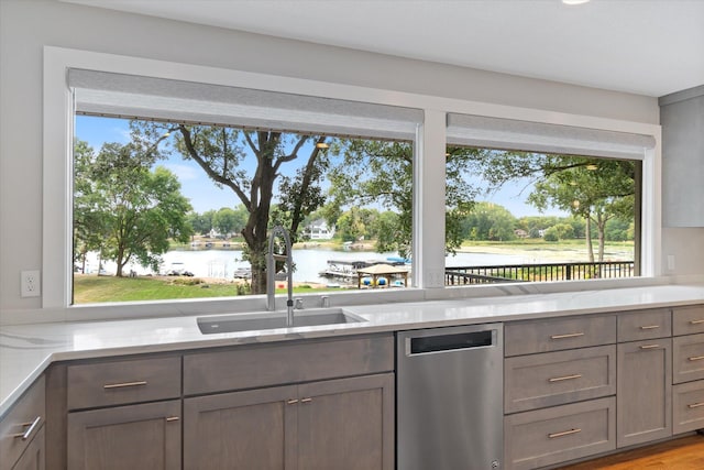 kitchen with sink, stainless steel dishwasher, light stone counters, a water view, and light wood-type flooring