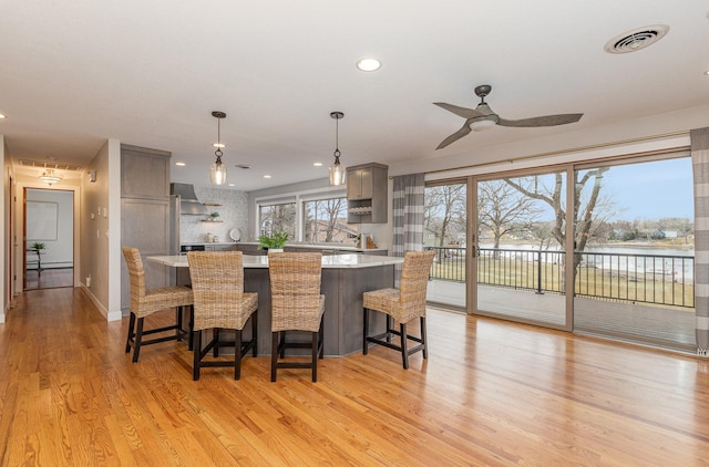 kitchen with gray cabinets, a breakfast bar, pendant lighting, a water view, and light wood-type flooring