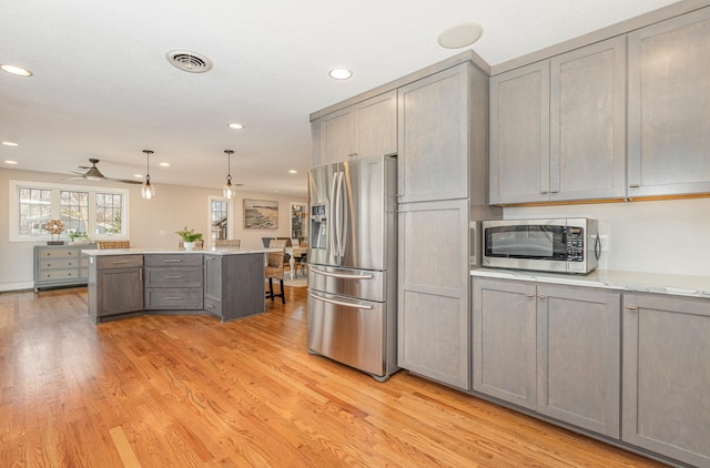 kitchen with light hardwood / wood-style flooring, gray cabinets, hanging light fixtures, stainless steel appliances, and light stone counters