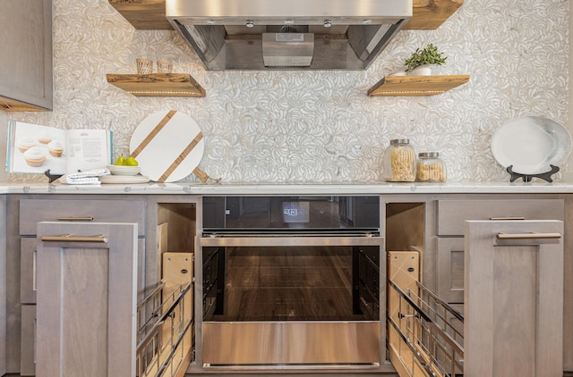 kitchen with light stone countertops, stainless steel oven, gray cabinetry, and wall chimney range hood