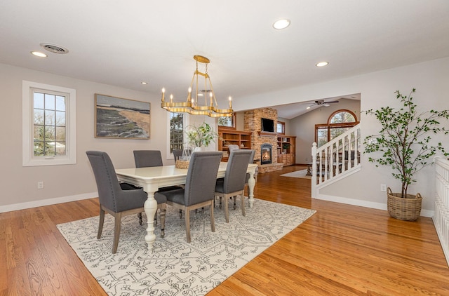 dining space featuring lofted ceiling, plenty of natural light, a stone fireplace, and light wood-type flooring