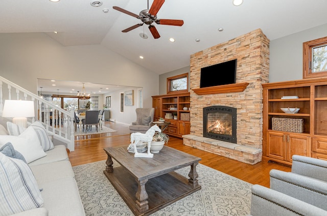 living room featuring ceiling fan with notable chandelier, high vaulted ceiling, a stone fireplace, and light hardwood / wood-style floors