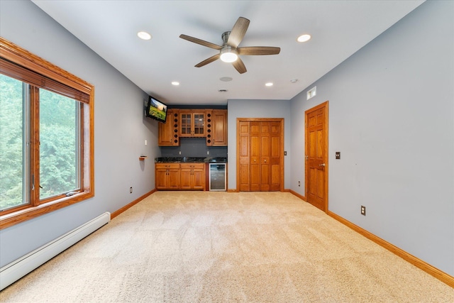 unfurnished living room featuring a baseboard radiator, wine cooler, bar, light colored carpet, and ceiling fan