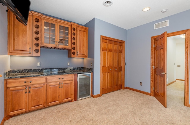 kitchen featuring light colored carpet, beverage cooler, and dark stone countertops