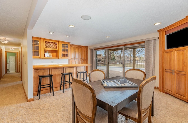 dining area featuring light colored carpet, a textured ceiling, and indoor bar