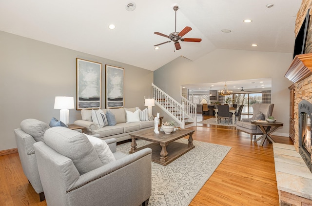 living room with wood-type flooring, a stone fireplace, ceiling fan with notable chandelier, and lofted ceiling