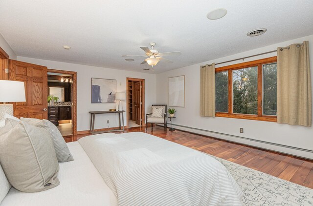 bedroom with ceiling fan, a baseboard heating unit, ensuite bathroom, wood-type flooring, and a textured ceiling