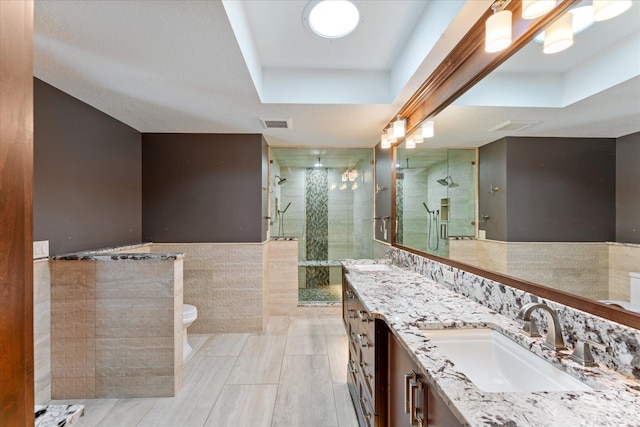 bathroom with vanity, a raised ceiling, tile walls, and walk in shower