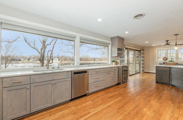 kitchen featuring pendant lighting, sink, beverage cooler, stainless steel dishwasher, and light hardwood / wood-style flooring