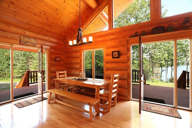 dining space featuring a healthy amount of sunlight, high vaulted ceiling, log walls, and light wood-type flooring