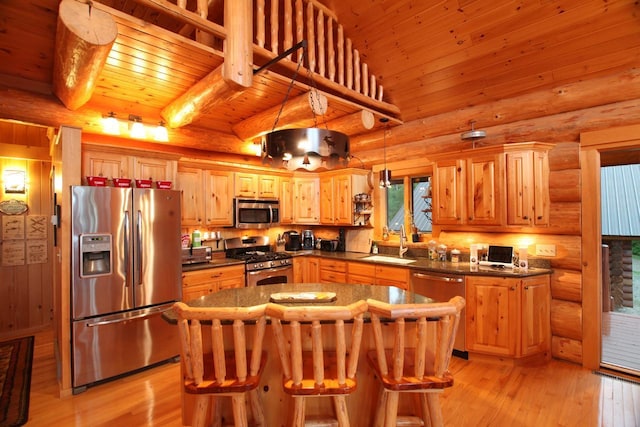 kitchen with decorative light fixtures, appliances with stainless steel finishes, light hardwood / wood-style floors, log walls, and a center island