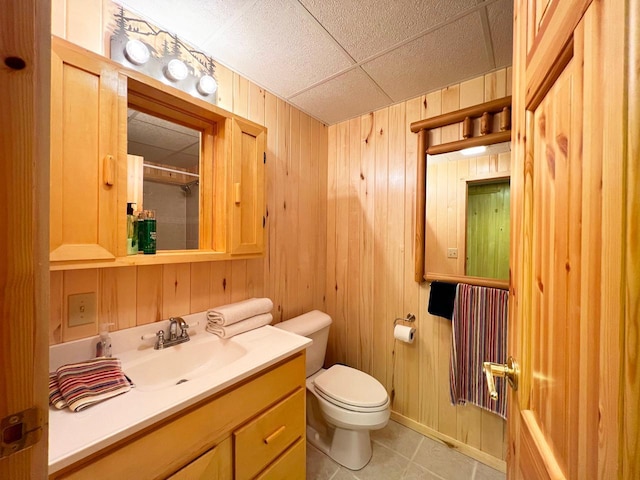 bathroom featuring a drop ceiling, oversized vanity, wood walls, toilet, and tile floors