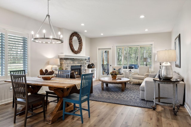 dining area with an inviting chandelier, a stone fireplace, and light hardwood / wood-style floors