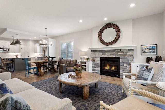 living room with an inviting chandelier, a stone fireplace, and light wood-type flooring