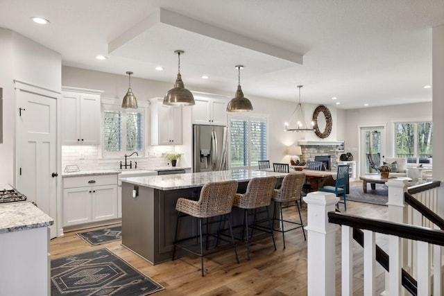 kitchen with a stone fireplace, light stone counters, stainless steel fridge, and white cabinetry