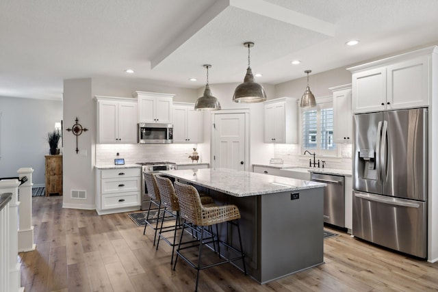 kitchen featuring light wood-type flooring, appliances with stainless steel finishes, white cabinets, and decorative backsplash