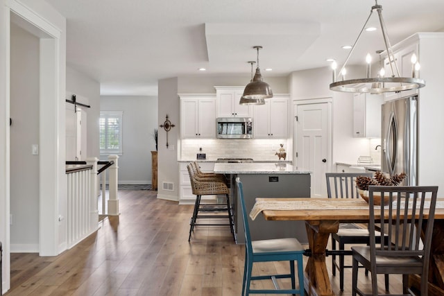 dining area featuring a barn door, wood-type flooring, and an inviting chandelier