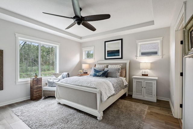 bedroom with wood-type flooring, a raised ceiling, and ceiling fan