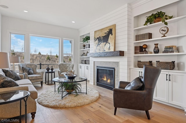 living room with built in shelves, a tiled fireplace, and light hardwood / wood-style floors