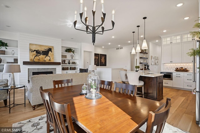 dining room with a notable chandelier, built in features, light hardwood / wood-style floors, and sink