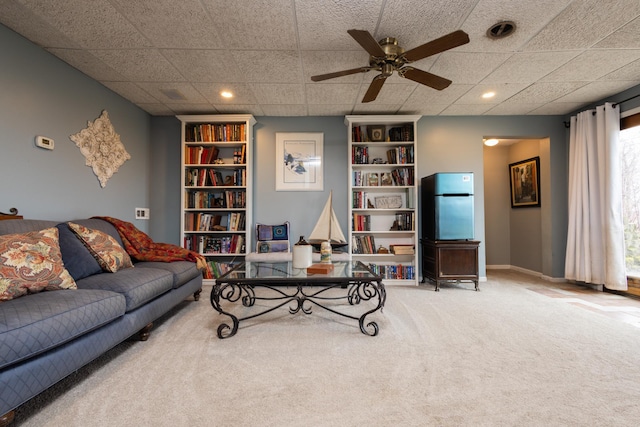 living room with carpet, a paneled ceiling, built in features, and ceiling fan