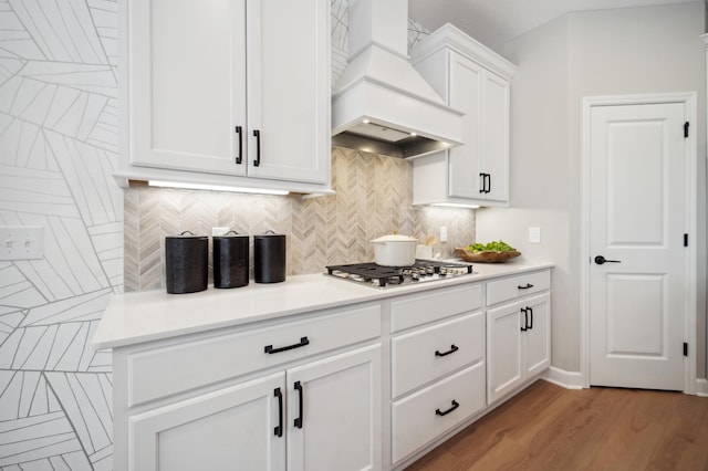 kitchen with premium range hood, tasteful backsplash, stainless steel gas cooktop, white cabinets, and light wood-type flooring