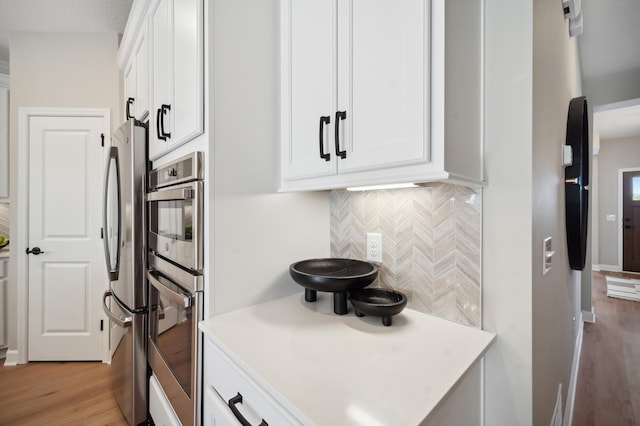 kitchen with white cabinets, backsplash, light wood-type flooring, and stainless steel appliances