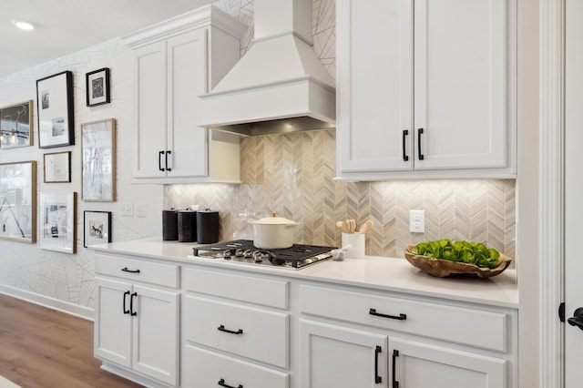 kitchen featuring premium range hood, light hardwood / wood-style floors, tasteful backsplash, stainless steel gas cooktop, and white cabinets