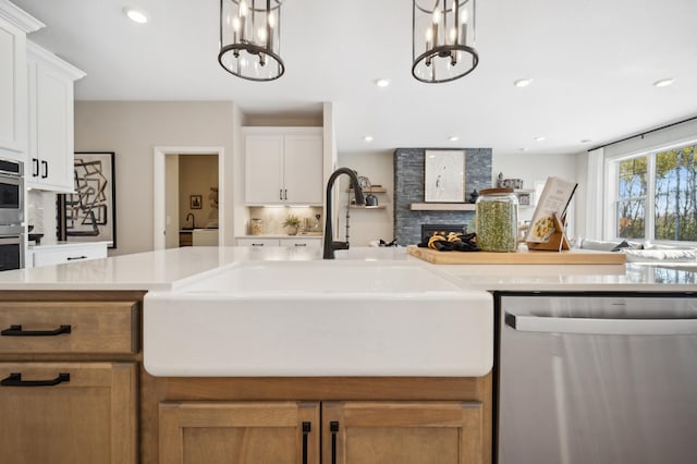 kitchen featuring a stone fireplace, stainless steel appliances, white cabinetry, pendant lighting, and a chandelier