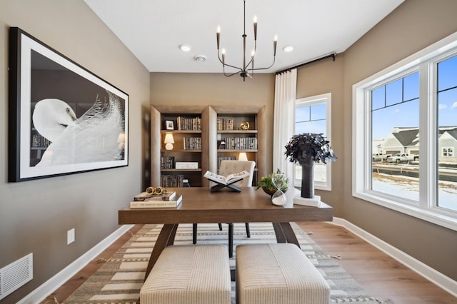 home office featuring built in features, an inviting chandelier, a healthy amount of sunlight, and hardwood / wood-style floors