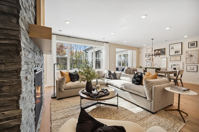 living room with an inviting chandelier, light hardwood / wood-style floors, and a stone fireplace